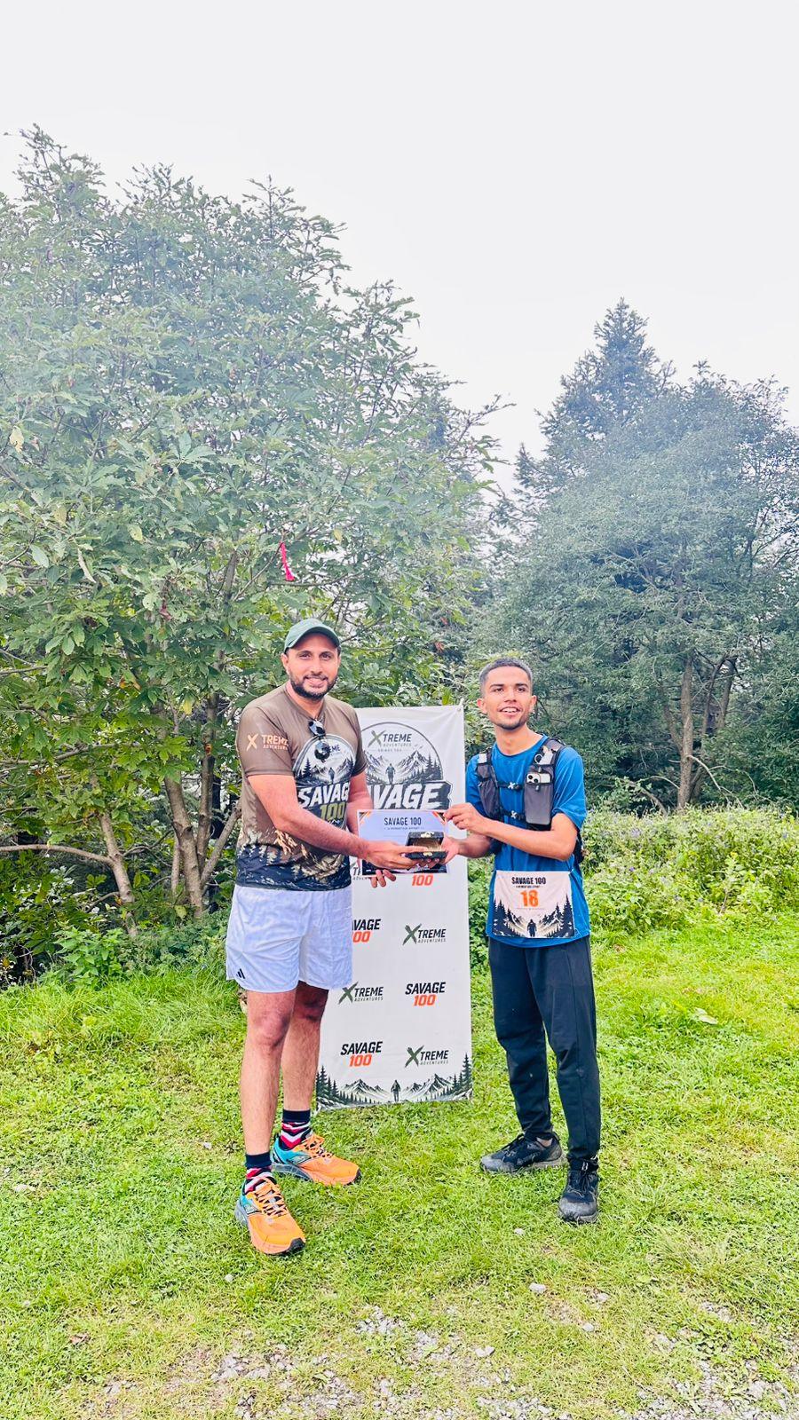The organiser handing a certificate to a finisher in a blue top and dark trousers, mist filling the trees behind