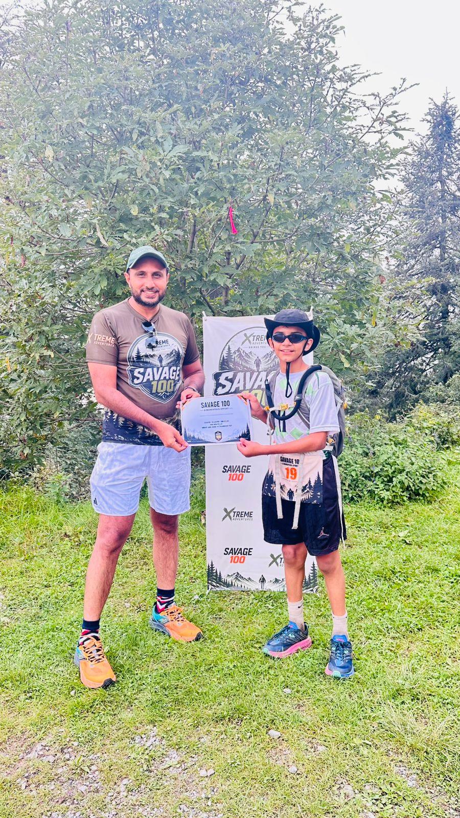 A second frame of the presentation to the young finisher in the black cap, both holding the branded banner up to the camera